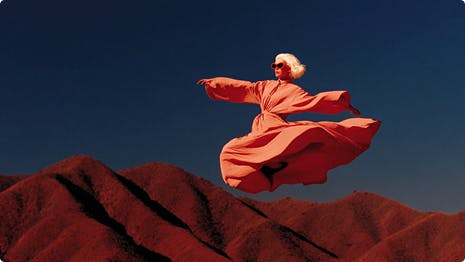 Женщина в розовом платье прыгает над красными холмами пустыни